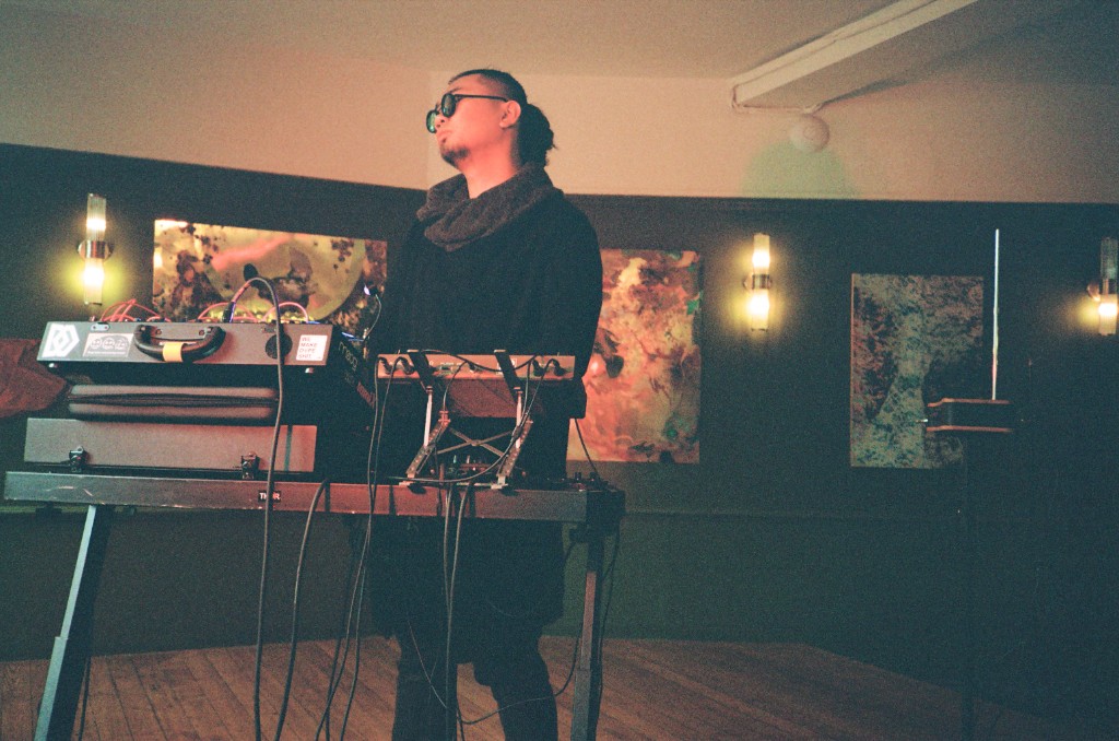 Artist with modular synthesizer and electronic instruments in a dimly lit studio